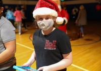 Girl in Santa hat wearing mask, standing inside gymnasium.