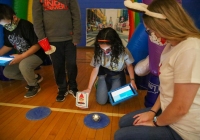 A group of people gathered around a table with sphero robots, engaged in an activity that involves using smartphones to