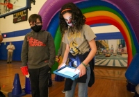 Two people standing in front of a colorful inflatable tunnel at an indoor event, one person holding a tablet and the other