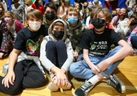 Five people wearing masks sitting on a floor in a gymnasium.