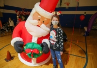 Girl posing next to large inflatable santa claus balloon in gymnasium.