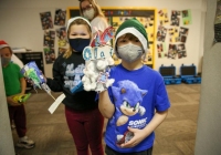 Two children in a classroom wearing masks, holding stuffed animals.