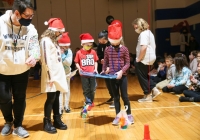 Children in santa hats playing with spheros on a gym floor.