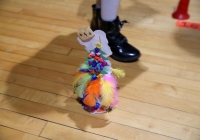 A person in a costume stands next to a colorful feathered object on the floor.
