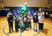 Children in masks posing with a large green Christmas tree decoration.