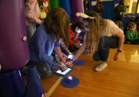 Two people standing in a room with purple walls and inflatable structures, looking at electronic devices on the floor.